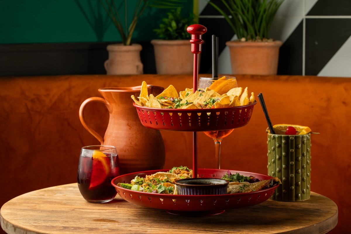 A vibrant red tiered tray filled with tortilla chips and tacos surrounded by Mexican cocktails